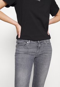 Jean en denim gris avec une légère décoloration, design à cinq poches, fermeture à bouton à l'avant, associé à un T-shirt noir à manches courtes.