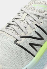 Sapatilha atlética cinza claro com parte superior em malha tecida, atacadores cinza claro, design de logotipo preto e detalhe do solado em neon verde.