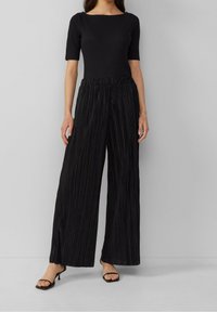 Haut noir côtelé à manches courtes associé à un pantalon noir plissé à jambes larges. La tenue présente une finition texturée et une taille élastique.