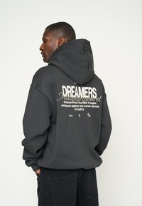 Zwarte hoodie met een ontspannen pasvorm. Heeft witte tekst en ontwerpen op de achterkant, ribbelmanchetten en een zachte textuur.