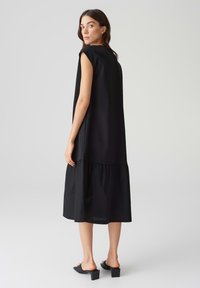 Schwarzes ärmelloses Kleid mit gestaffeltem Saum, aus leichtem Stoff gefertigt. Sanfte Textur, lockere Passform und einfaches Design. Quadrat-Ausschnitt.