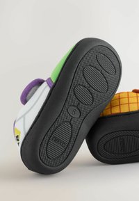 Colorful children's slippers with a patterned fabric upper in white, green, purple, and yellow; textured black rubber soles with grip patterns.