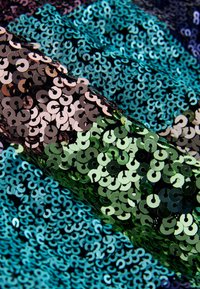 Paljettstyg med överlappande cirkulära paljetter i nyanser av teal, grönt och svart, som skapar ett skimrande, texturerat utseende.