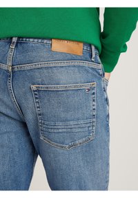 Modré denimové džínsy s koženou zadní nášivkou s logem "TOMMY HILFIGER". Džínsy mají standardní švy a design zadní kapsy.