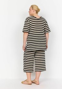 Gestreepte gebreide outfit met een T-shirt met korte mouwen en cropped broeken in beige en zwart. Hoogtepunten zijn een V-hals en zijslits.