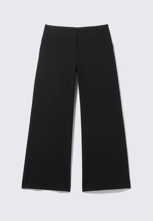Pantalons noirs à jambes larges en tissu lisse, avec un design minimaliste et sans matériel ou motifs visibles, posés à plat sur un fond clair.