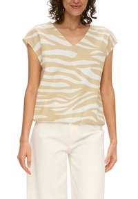 Beige Oberteil mit weißen Zebra-Streifen, V-Ausschnitt und kurzärmeligen Flügelärmeln. Aus leichtem Stoff, lockere Passform, kombiniert mit weißen weiten Hosen.