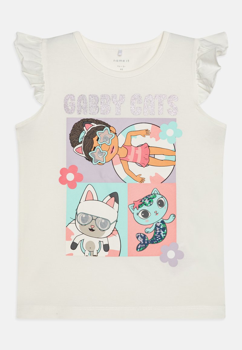 Hvit lin skjorte med volanger på ermene, prydet med tegneseriefigurer i fargerike firkanter. Teksten leser "GABBY CATS" i glitrende bokstaver.