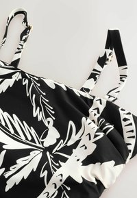 Čierno-biele šaty bez rukávov s nastaviteľnými ramienkami, ktoré majú výrazný abstraktný kvetinový vzor na hladkej látke.