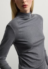 T-shirt gris à manches longues avec un col montant, fabriqué en tissu doux et lisse. Il présente une silhouette ajustée et une texture subtile.