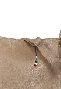 Beige, gestructureerde leren handtas met een platte riem en zilveren hardware. Heeft een kleine Italiaanse vlagbedel bevestigd aan de riem.
