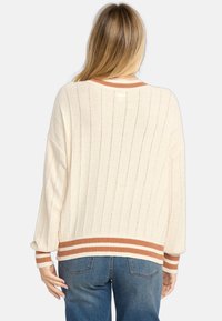 Pull crème à texture côtelée, avec des manches larges et des finitions à rayures marron et blanc au niveau des poignets et de l'ourlet. La vue de dos montre des lignes verticales.