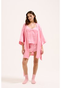 Ensemble de pyjama en satin rose comprenant un débardeur, un short et un peignoir style kimono avec des manches larges. Tissu texturé, design simple et accents délicats.