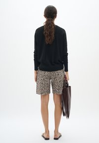 Un pull noir, un short à imprimé léopard et un sac fourre-tout marron. Tissu tricoté lisse, coupe décontractée, short mi-cuisse, sandales plates.