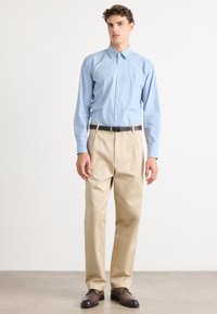 Camisa azul clara de botões, calças bege, cinto preto, sapatos castanhos; tecido suave, corte ajustado, colarinho clássico, sem padrões visíveis.