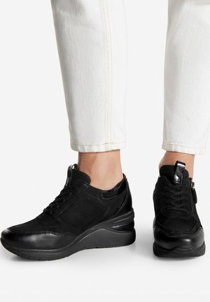 Zapatos deportivos negros con una combinación de materiales lisos y texturizados, que presentan un tacón de cuña, cordones y detalle de cremallera lateral.