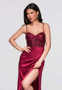 Robe de soirée en satin rouge avec un corsage structuré orné de sequins et des bretelles fines, présentant une fente haute à la cuisse pour une élégance accrue.