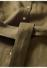 Brun hørskjorte med en blød tekstur, der har en knaplukning foran, et bundet bælte og perleagtige knapper.