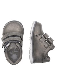 Scarpe per bambini di colore grigio metallico con doppie fascette in Velcro, punta tonda, superficie testurizzata e una suola in gomma bianca con un motivo a rilievo.