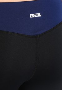 Nära bild av svarta och marinblå träningsleggings med en vit "B DRY"-logotyp på den marinblå midjebandet.