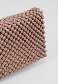 Pochette texturée recouverte de petites perles rondes brillantes de couleur rose pâle. Présente une forme rectangulaire géométrique. Sans éléments métalliques visibles.