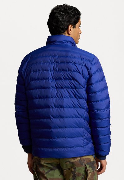 Casaco puffer azul com um design de matelassé em fileiras, gola alta e punhos elásticos, combinado com calças cargo camufladas.