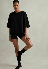 Černé oversized tričko s krátkým rukávem, v kombinaci s černými šortkami a černými ponožkami po kolena; hladká látka a uvolněný střih.