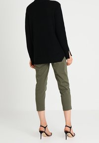 Maglione oversized nero a coste con spacchi laterali, abbinato a un pantalone cropped verde oliva con motivo testurizzato e tacchi neri con fasce.