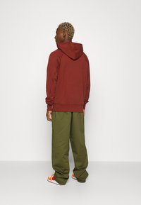 Mörkröd huvtröja med dragsko, ribbade muddar och nederkant, parat med lösa olivgröna byxor och orange- och vita sneakers.