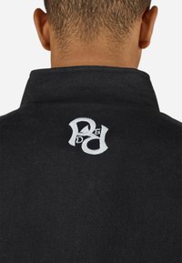 Sort polo shirt med høj krave og et broderet hvidt logo på ryggen. Blød tekstur med et rent, minimalistisk design.