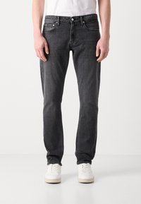 Črne denim hlače s ravnim krojem, ki vključujejo pet žepov, zadrgo in kontrastno šivanje. Nosi se z belimi supergami.