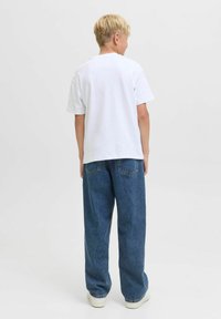 T-shirt en coton blanc et jeans en denim bleu ample. Les jeans présentent des poches arrière et une texture délavée. Les chaussures sont blanches avec une semelle plate.
