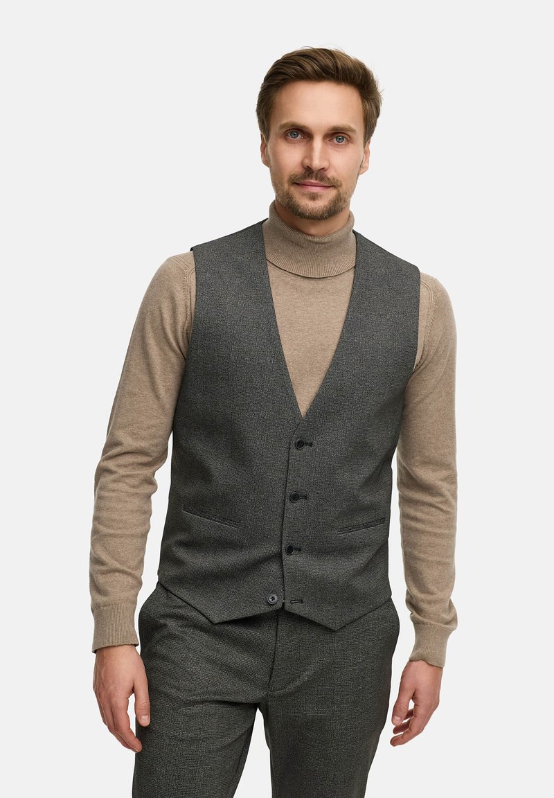 Grå vest med subtil tekstur, med V-hals, fem knapper og sidelommer, båret over en beige rullekrave og matchende bukser.