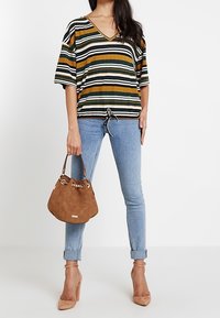 Top de cuello en V a rayas con dobladillo ajustable, acompañado de jeans skinny azul claro y un bolso de ante marrón con detalles en cadena.