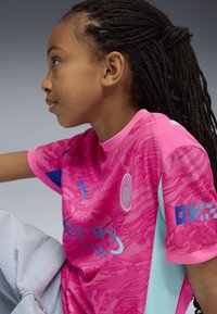 Rosa sportströja med en texturerad design och blå detaljer och logotyp. Kort ärm och hög krage. Materialet verkar lätt och andningsbart.