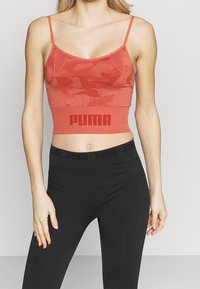 Skåret sports-bh i rød med camouflage-mønster, justerbare stropper og en bred PUMA-logo-bånd forneden. Glat tekstur.