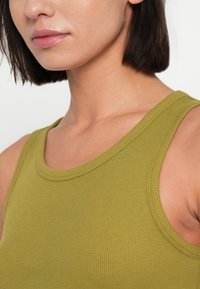 Λαδί πράσινο ριμπ αμάνικο τοπ με στρογγυλή λαιμόκοψη και φαρδιές τιράντες, που αναδεικνύει μια ομαλή υφή και εφαρμοστή γραμμή.