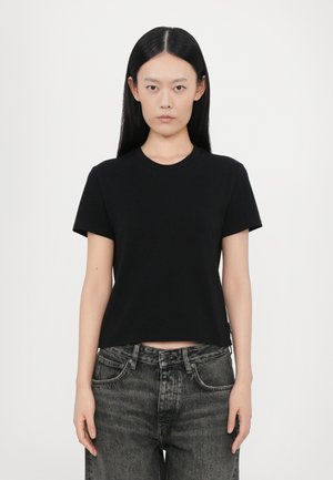 Black short-sleeve cotton t-shirt with a round neckline, fitted design, and a cropped cut. Paired with high-waisted dark denim jeans.
