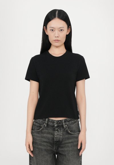 Black short-sleeve cotton t-shirt with a round neckline, fitted design, and a cropped cut. Paired with high-waisted dark denim jeans.