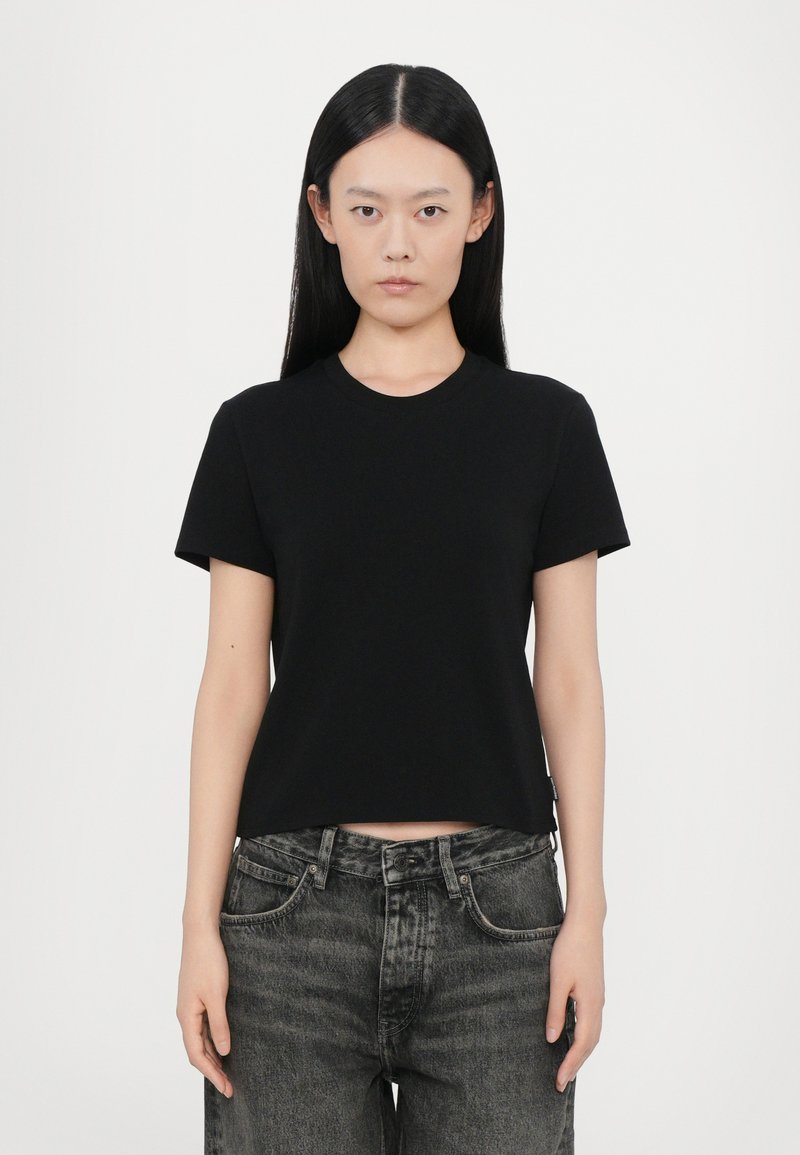 Black short-sleeve cotton t-shirt with a round neckline, fitted design, and a cropped cut. Paired with high-waisted dark denim jeans.