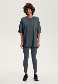 Överdimensionerad mörkgrå kortärmad skjorta i kombination med tajta mörkgrå leggings och svarta träningsskor, med en mjuk struktur och avslappnad design.