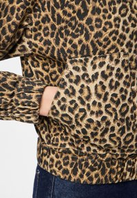 Luvtröja med leopardsmönster i avslappnad passform, med elastiska ärmslut och fåll. Tyget har en strukturerad, mjuk känsla, med djup svart och varm brun ton.