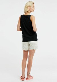 Top senza maniche nero, pantaloni beige chiaro, e sandali rosa. Il top presenta un collo rotondo e i pantaloni hanno risvolti.