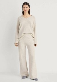 Beige gebreide trui met een V-hals, gecombineerd met brede beige gebreide broek. Beiden hebben een zachte textuur en een ontspannen pasvorm.