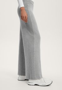 Sive široke pletene hlače z navpično rebrastim vzorcem ob straneh, v kombinaciji z belimi športnimi čevlji. Gladka tekstura, sproščen kroj.