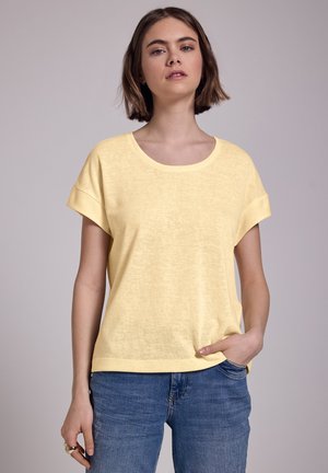 Geel T-shirt met korte mouwen, een ontspannen pasvorm, ronde hals en omgeslagen mouwen, gemaakt van een lichte, gestructureerde stof. Gepaard met blauwe jeans.