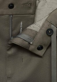 Olive green jacket interior with a textured lining, featuring a zipper pocket, and black buttons. Durable fabric with robust stitching details.