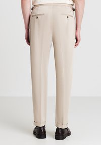 Beige maßgeschneiderte Hosen aus glattem Stoff, mit zwei Gesäßtaschen mit Knöpfen, geraden Beinen und umgeschlagenen Säumen an den Knöcheln.