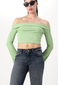 Svijetlozeleni rebrasti crop top s dizajnom bez naramenica i dugim rukavima, u kombinaciji s tamnim trapericama u klasičnom petokutetnom stilu.