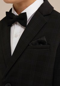 Černá kára smokingová bunda s saténovým černým kapesníčkem, bílou košilí a černým motýlkem. Texturovaná tkanina, střih na míru.